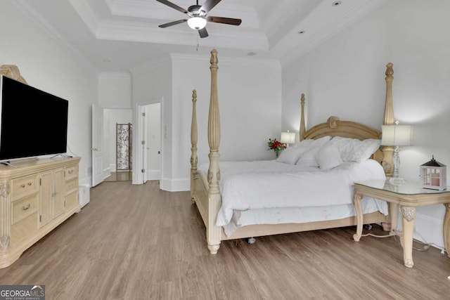 bedroom with crown molding, ceiling fan, baseboards, a tray ceiling, and wood finished floors