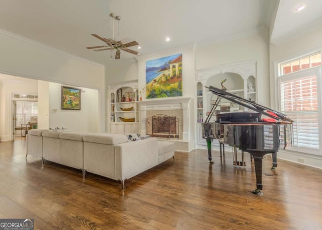 living room with built in shelves, a ceiling fan, wood finished floors, a high end fireplace, and crown molding