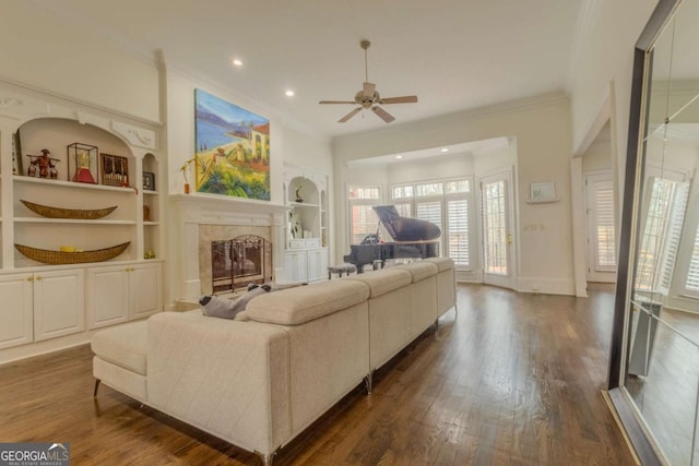 living room with dark wood-type flooring, baseboards, crown molding, built in features, and a fireplace