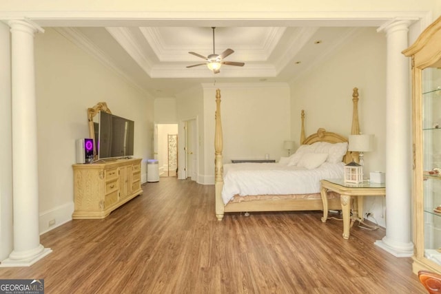 bedroom with a raised ceiling, wood finished floors, and ornate columns