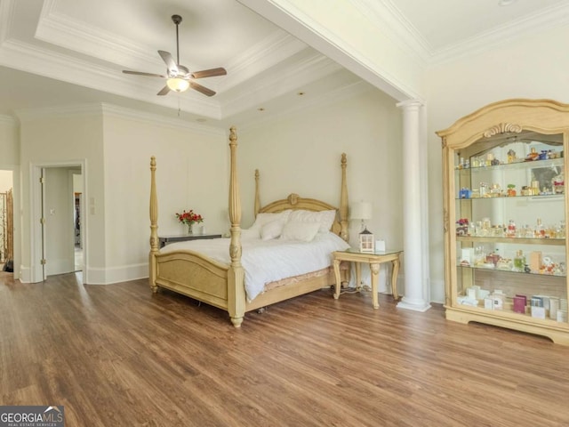 bedroom with a tray ceiling, wood finished floors, crown molding, and ornate columns