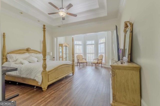 bedroom with a tray ceiling, wood finished floors, and ornamental molding