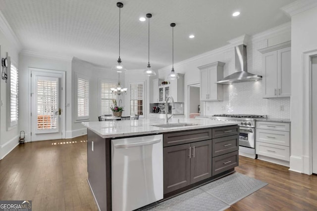 kitchen with dark wood finished floors, ornamental molding, a sink, appliances with stainless steel finishes, and wall chimney range hood