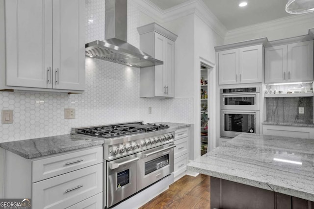 kitchen with appliances with stainless steel finishes, light stone countertops, wall chimney exhaust hood, and ornamental molding