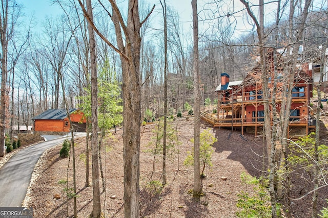 view of yard with aphalt driveway, a wooded view, and a wooden deck