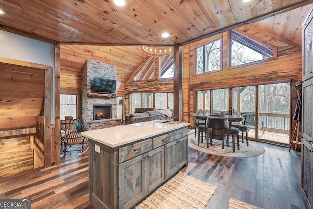 kitchen featuring a stone fireplace, high vaulted ceiling, wood ceiling, and wood walls