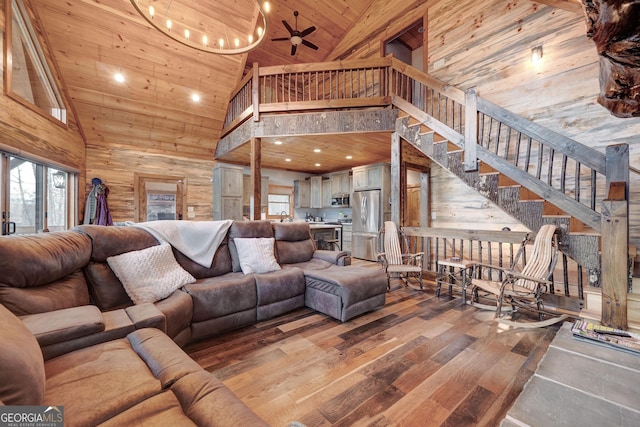 living room with wooden walls, wood finished floors, high vaulted ceiling, stairs, and wood ceiling