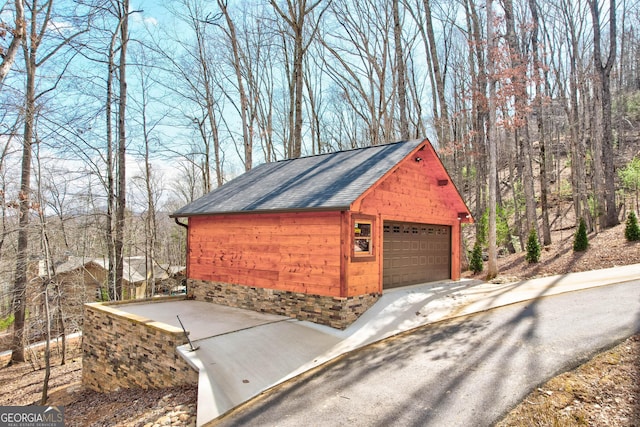 view of side of property featuring a garage, an outdoor structure, and a shingled roof