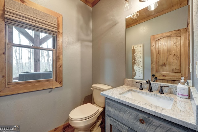 bathroom with toilet, vanity, and a textured wall