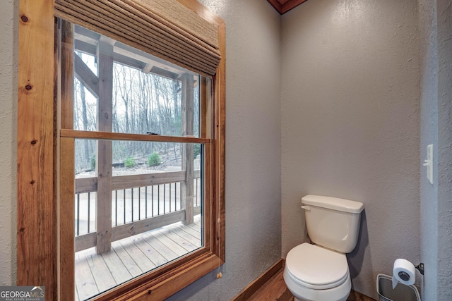 bathroom with wood finished floors, toilet, baseboards, and a textured wall