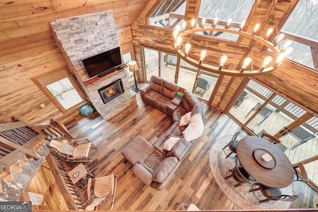 living room featuring wood walls, a stone fireplace, an inviting chandelier, wood finished floors, and high vaulted ceiling