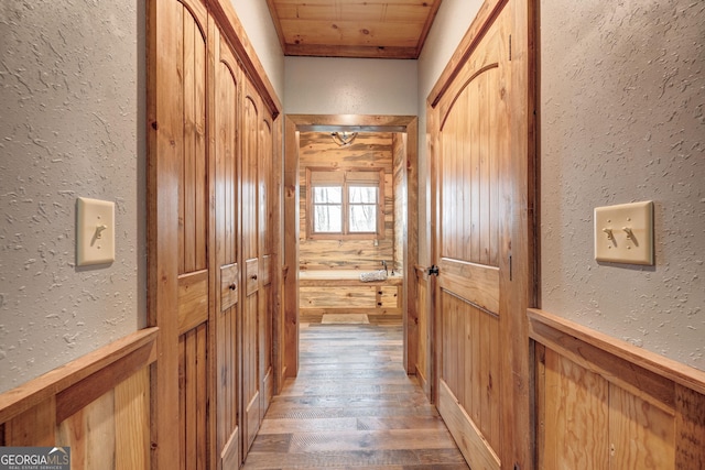 corridor featuring light wood finished floors, wooden walls, wainscoting, and a textured wall