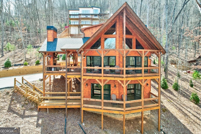 back of house with a wooden deck, a wooded view, and a chimney