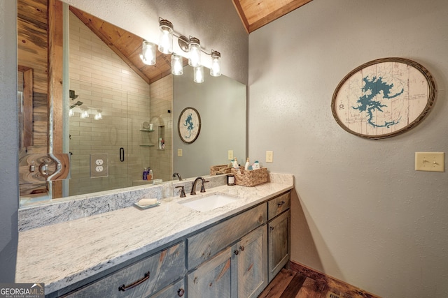 full bathroom with vanity, wood finished floors, baseboards, a stall shower, and vaulted ceiling