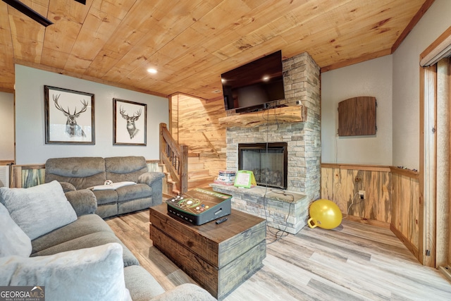 living room featuring wood finished floors, a stone fireplace, wooden ceiling, and wood walls