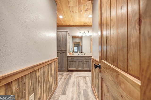 bathroom with vanity, wooden walls, wood finished floors, wainscoting, and wooden ceiling