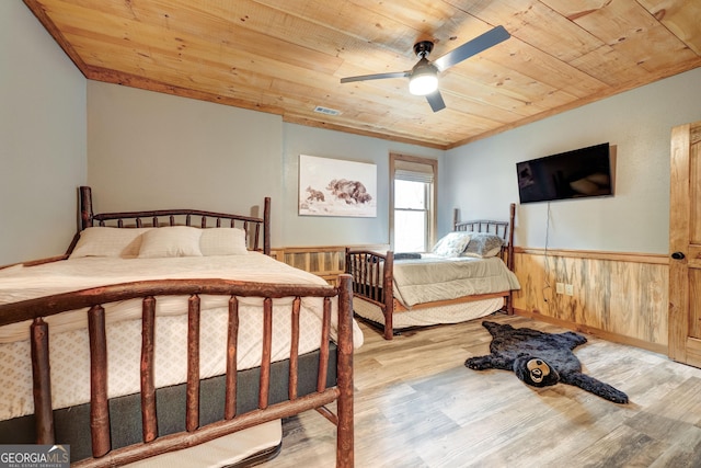 bedroom featuring wood finished floors, ceiling fan, wood walls, wainscoting, and wooden ceiling