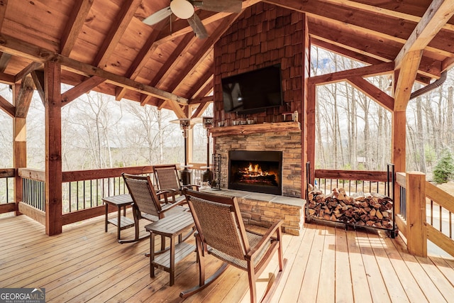 wooden terrace with an outdoor stone fireplace and ceiling fan