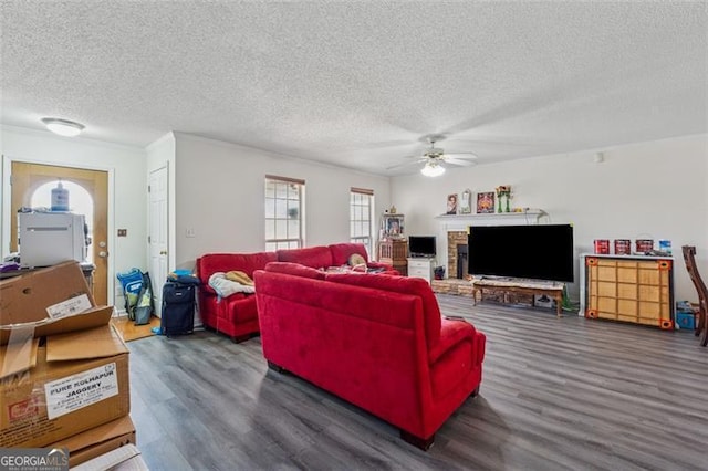 living room with a textured ceiling, a fireplace with raised hearth, wood finished floors, and a ceiling fan