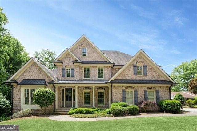 view of front of property featuring brick siding, covered porch, a front yard, and a standing seam roof