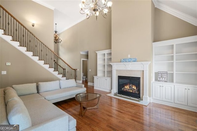 living area featuring crown molding, a chandelier, stairs, a fireplace, and wood finished floors