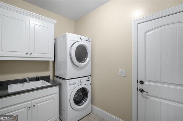 laundry room with cabinet space, stacked washing maching and dryer, baseboards, and a sink