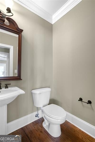 half bathroom featuring toilet, crown molding, baseboards, and wood finished floors