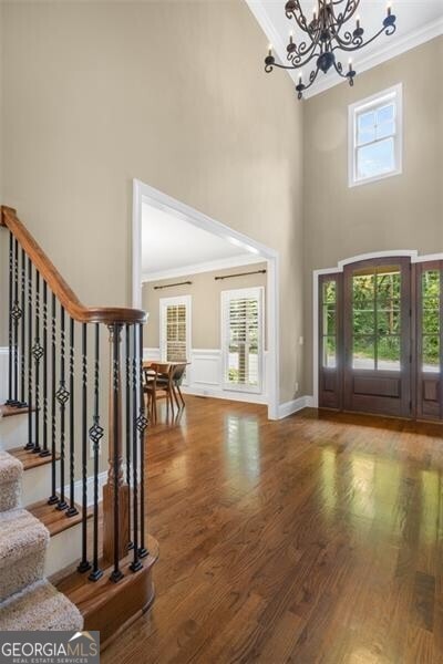 entrance foyer with a wealth of natural light, an inviting chandelier, wood finished floors, and crown molding