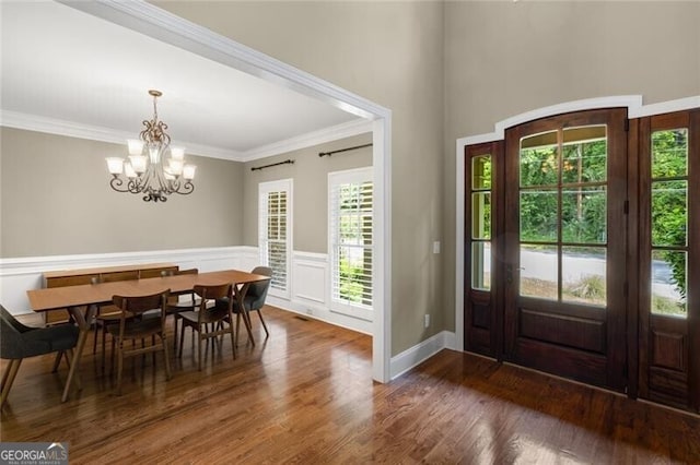 foyer entrance with crown molding, wood finished floors, a wainscoted wall, and a chandelier