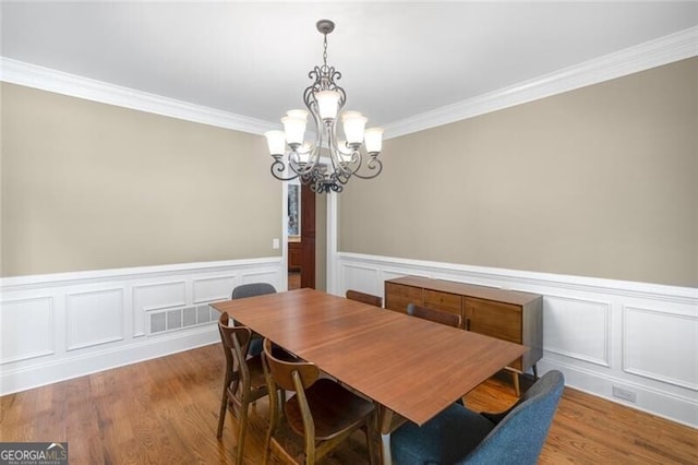 dining area with a wainscoted wall, an inviting chandelier, wood finished floors, and ornamental molding