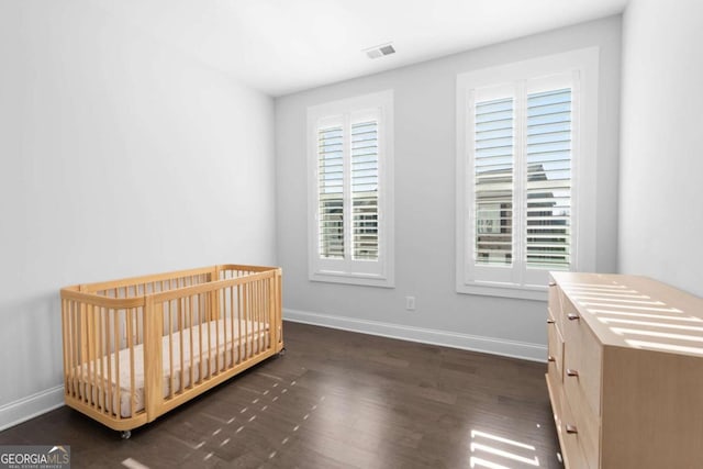 unfurnished bedroom with a crib, visible vents, baseboards, and wood finished floors