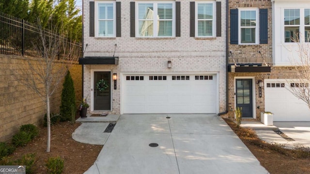 view of front of home featuring brick siding, an attached garage, driveway, and fence