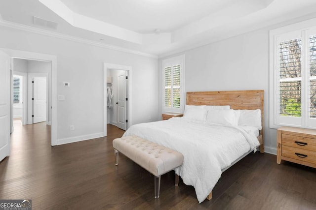 bedroom featuring dark wood finished floors, visible vents, baseboards, and a tray ceiling