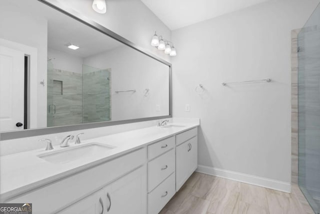 full bathroom with double vanity, a shower stall, baseboards, and a sink