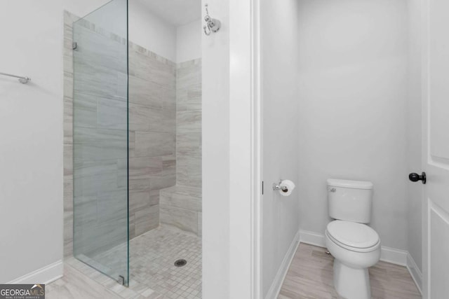 full bath with toilet, tiled shower, and baseboards