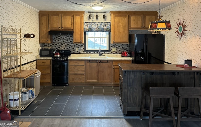 kitchen featuring brown cabinetry, wallpapered walls, a sink, black appliances, and under cabinet range hood