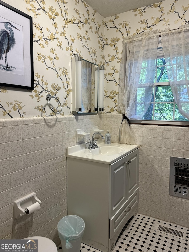 bathroom featuring toilet, heating unit, wainscoting, wallpapered walls, and vanity