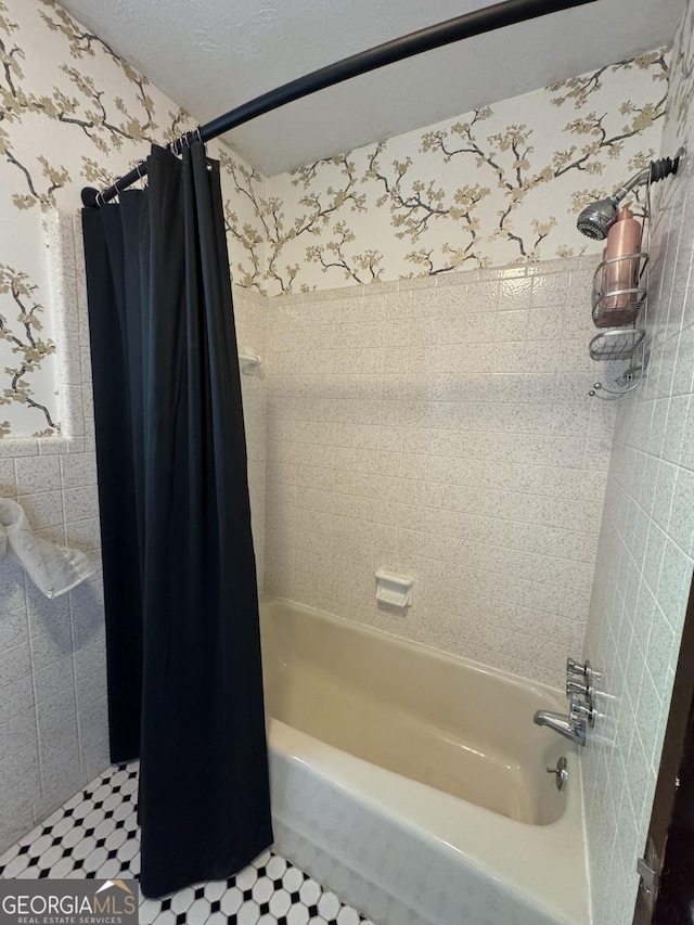 full bath with a textured ceiling, wallpapered walls, and shower / bathtub combination with curtain