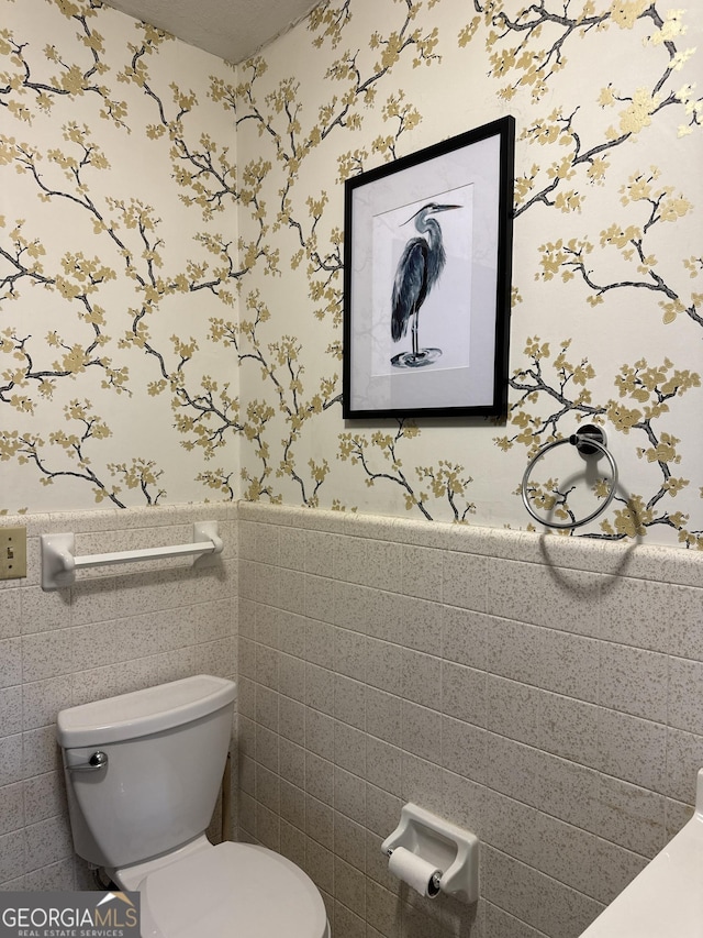 bathroom featuring a wainscoted wall, wallpapered walls, toilet, and tile walls
