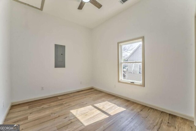 spare room with electric panel, baseboards, light wood finished floors, and ceiling fan