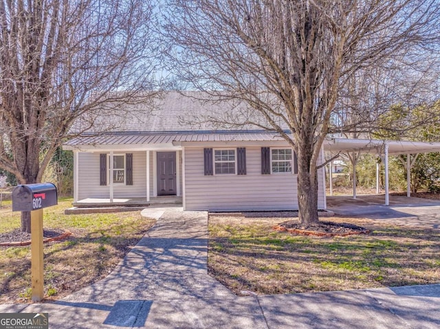 ranch-style home featuring a carport, covered porch, driveway, and metal roof