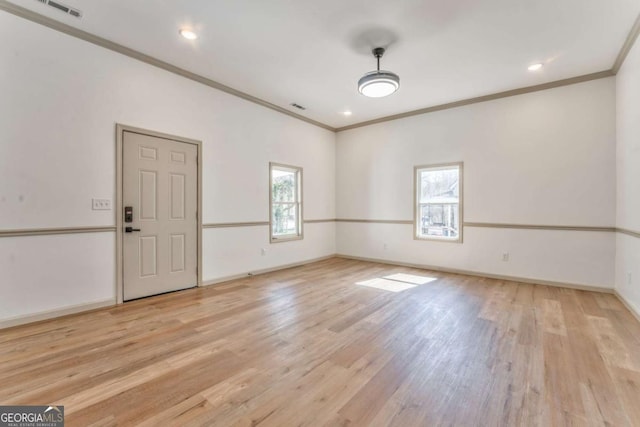 spare room with light wood-type flooring, baseboards, visible vents, and crown molding