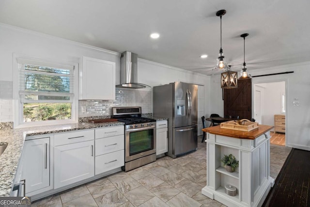 kitchen with a barn door, ornamental molding, white cabinets, stainless steel appliances, and wall chimney exhaust hood