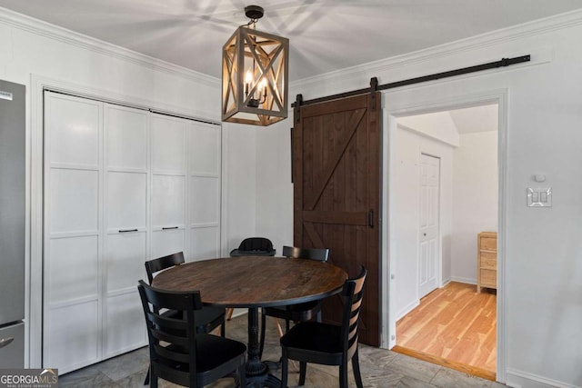 dining room with a barn door, wood finished floors, baseboards, and ornamental molding