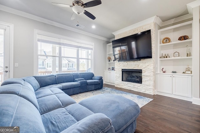 living area with dark wood-style floors, visible vents, ceiling fan, a stone fireplace, and crown molding