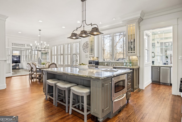 kitchen with stainless steel microwave, gray cabinetry, a kitchen island, crown molding, and light stone countertops