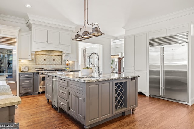 kitchen featuring high end appliances, an island with sink, gray cabinets, a sink, and crown molding