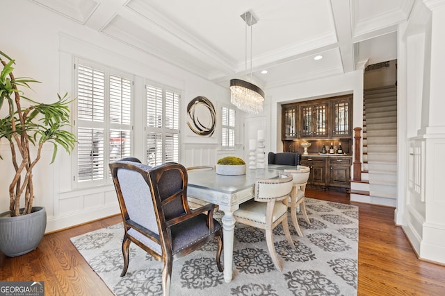 dining space with beam ceiling, a decorative wall, coffered ceiling, and wood finished floors