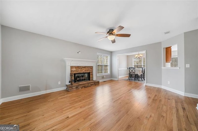 unfurnished living room with baseboards, visible vents, a fireplace, ceiling fan with notable chandelier, and light wood-type flooring