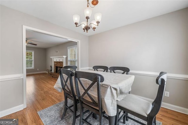 dining room with a chandelier, a stone fireplace, baseboards, and light wood-style floors